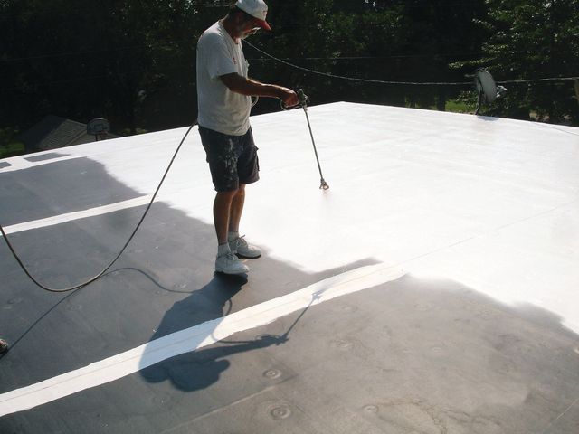 Person pressure-washes a white rooftop under bright sunlight, with hoses trailing behind.