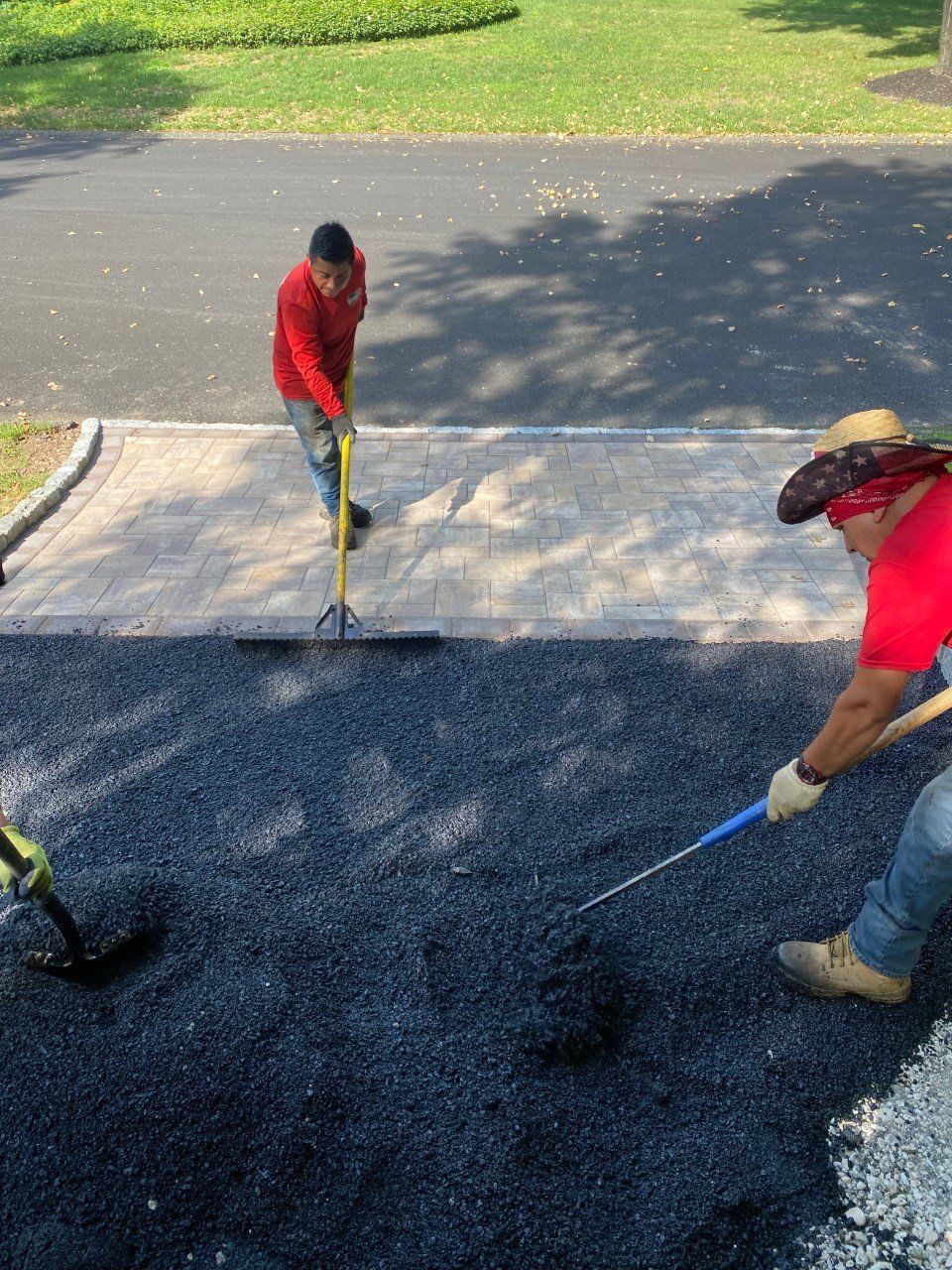 Two men are working on a driveway with a broom and rake