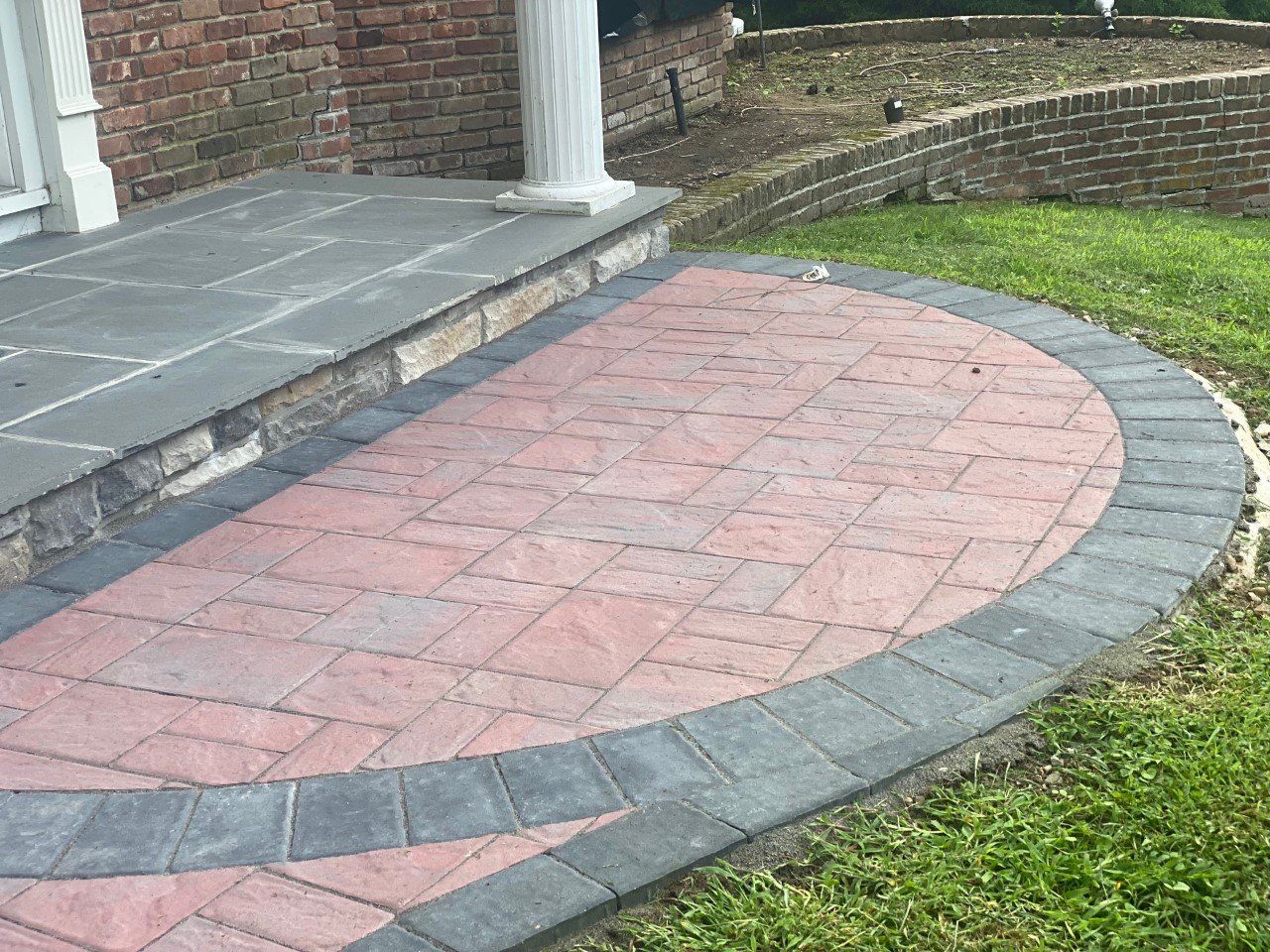 A brick walkway leading to a porch with a brick wall in the background.