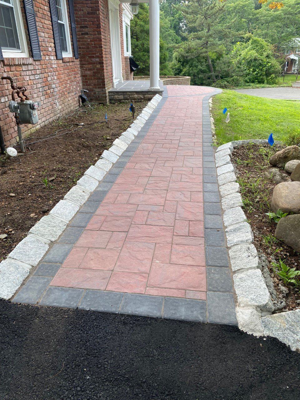 A brick walkway leading to a house with a brick building in the background.