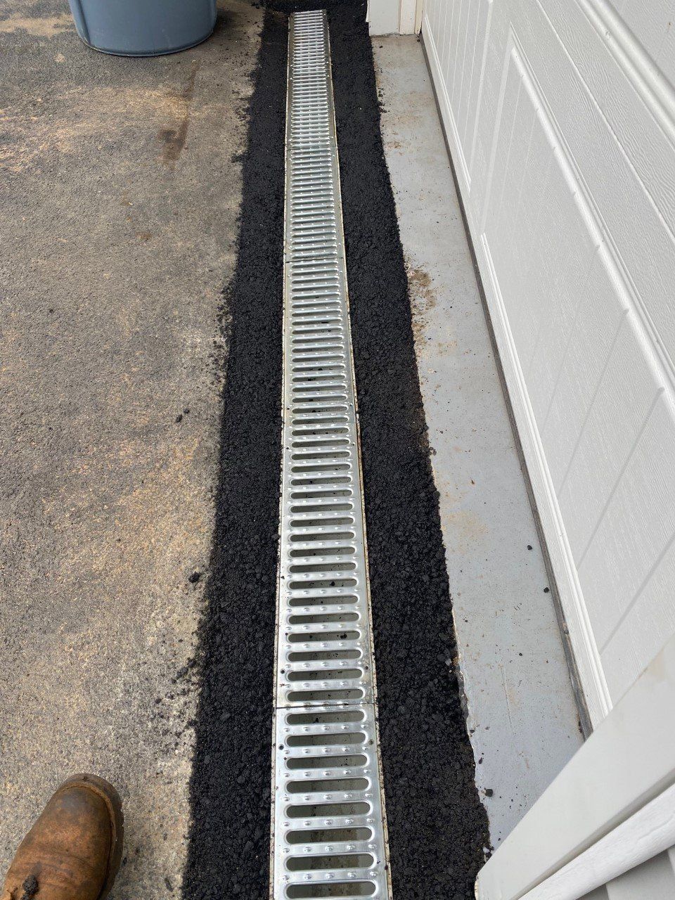 A drain is being installed next to a garage door