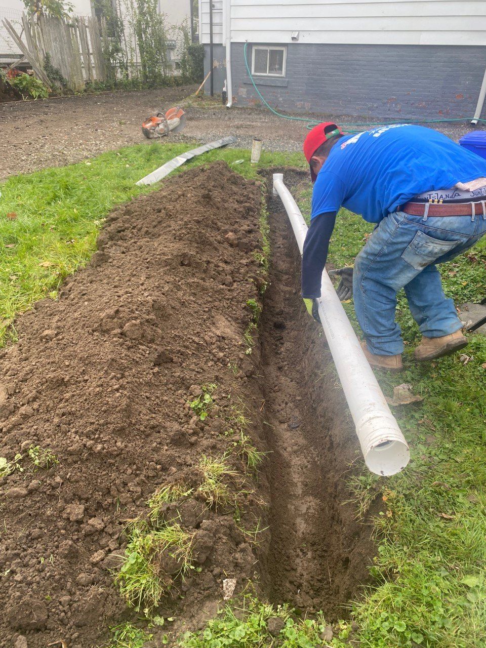 A man is digging a hole in the ground to install a drain pipe.