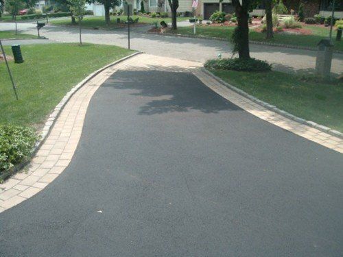 A black asphalt driveway with a brick curb