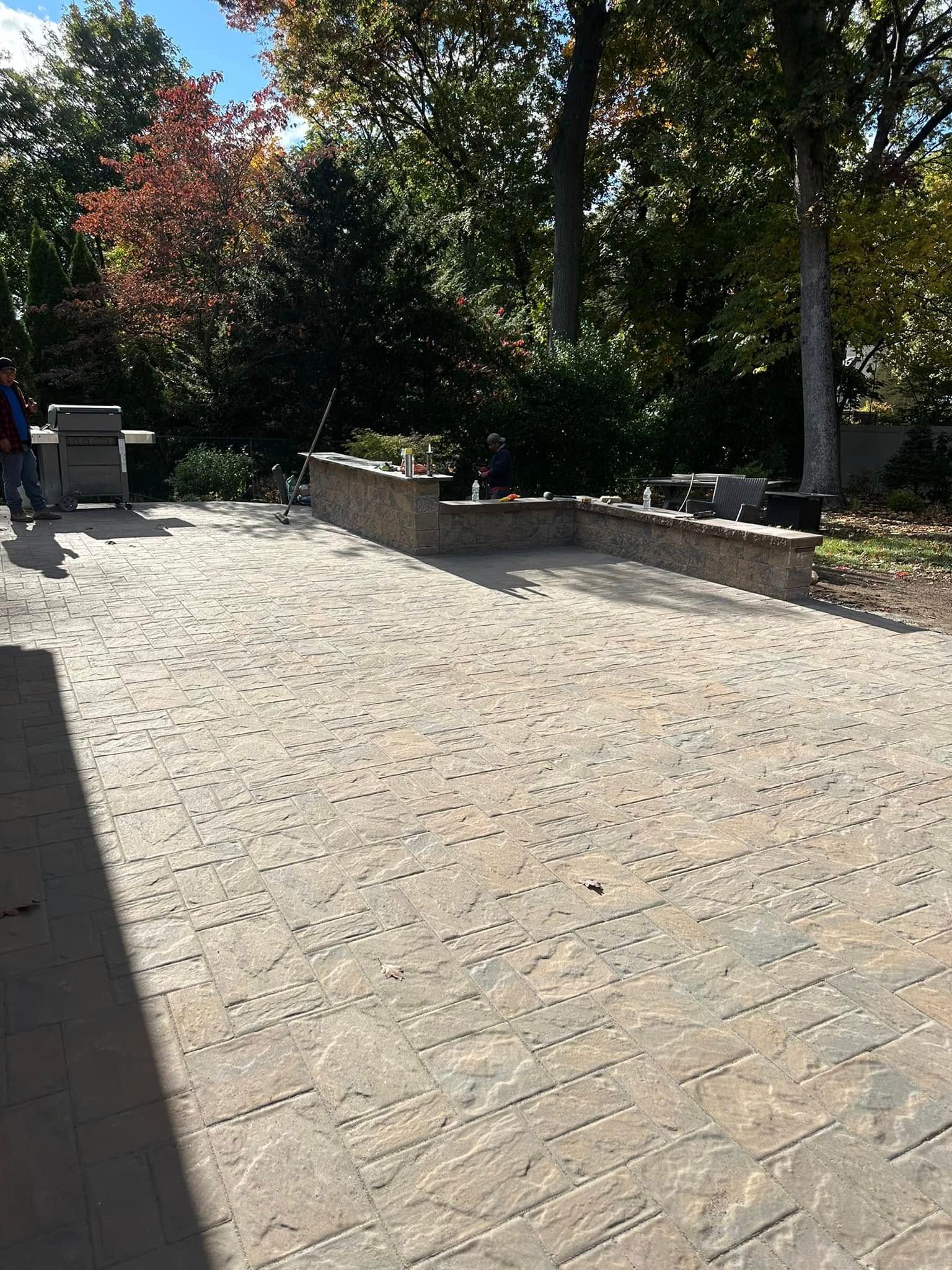 A brick patio with a grill and trees in the background.