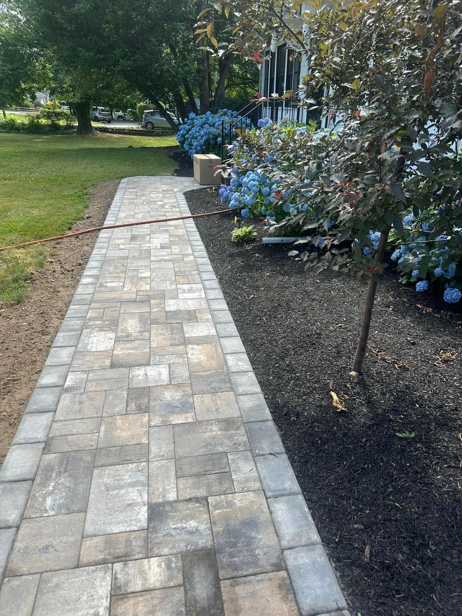 A brick walkway leading to a house surrounded by trees and bushes.