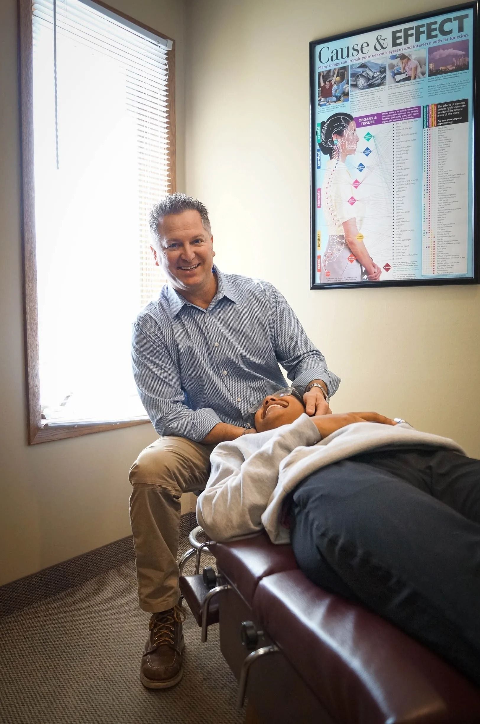 Chiropractor adjusting a patient's neck. Doctor smiles while patient lies on an examination table. Clinic interior.