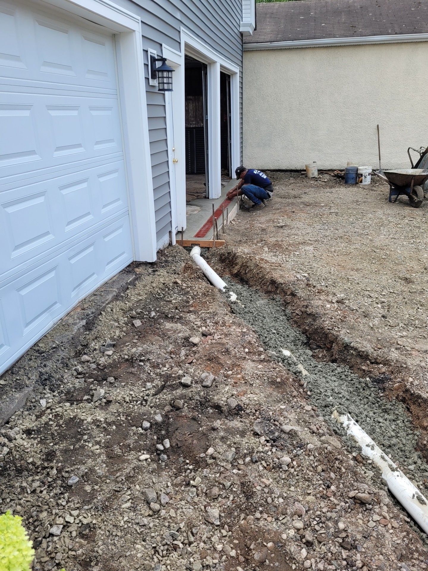 A man is laying pipes in the dirt in front of a garage door.