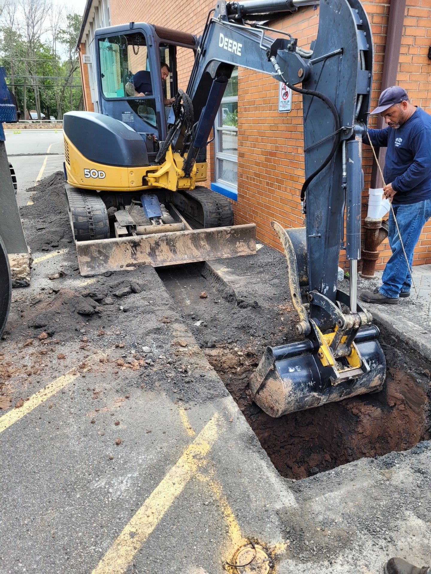 A man is standing next to an excavator digging a hole in the ground.