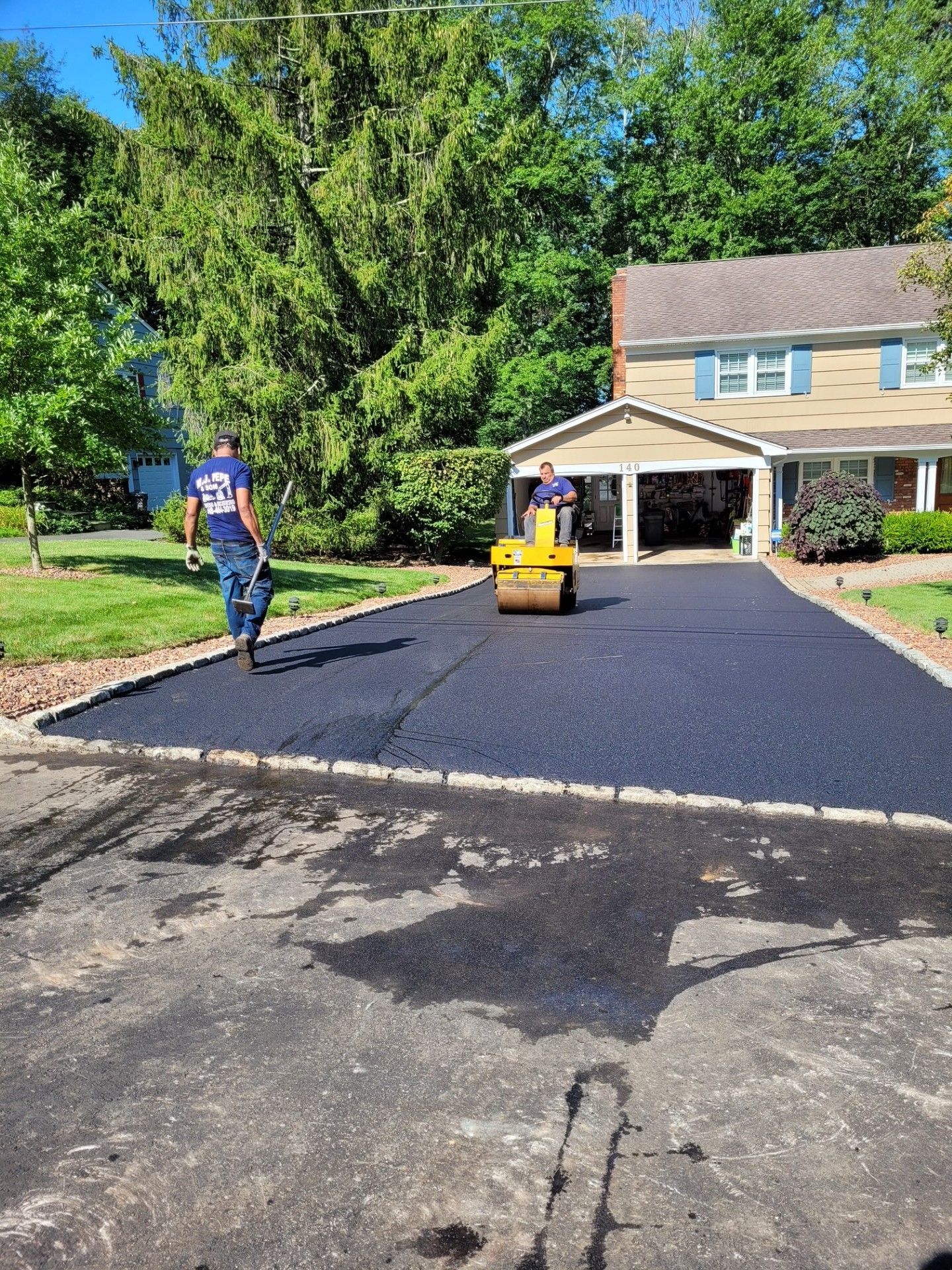 A man is walking down a driveway next to a yellow roller.
