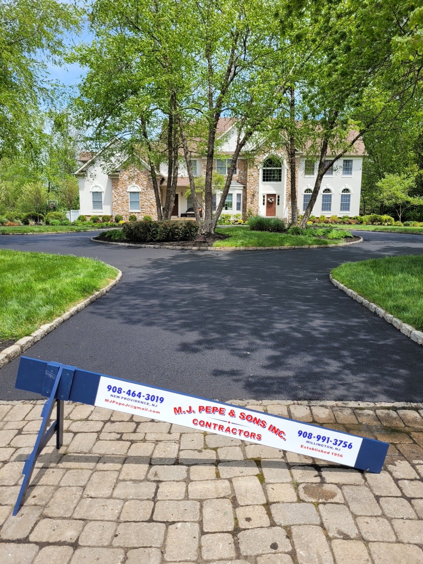 A large house with a brick driveway and a blue barrier in front of it.