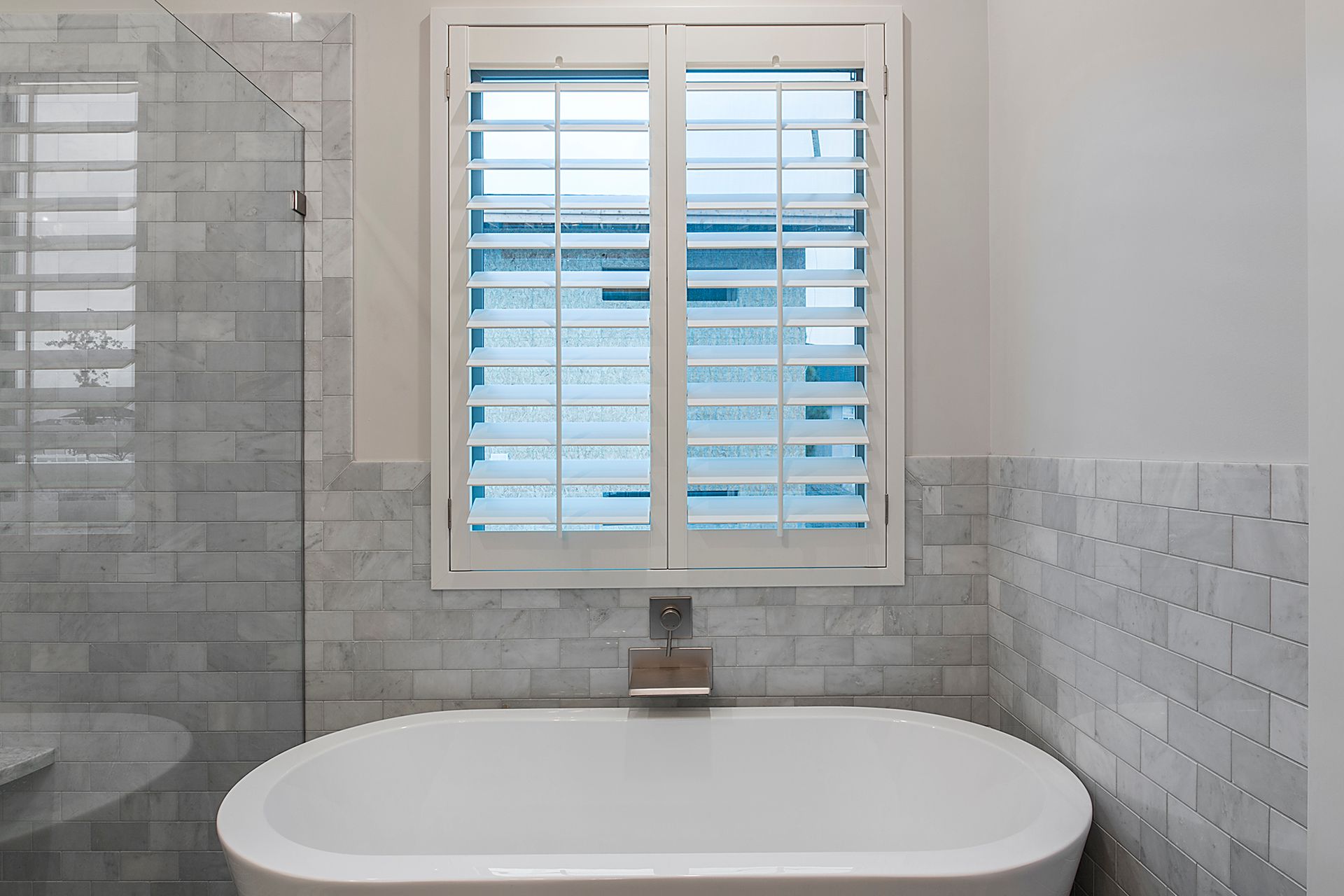 A bathroom with a bathtub and a window with shutters.