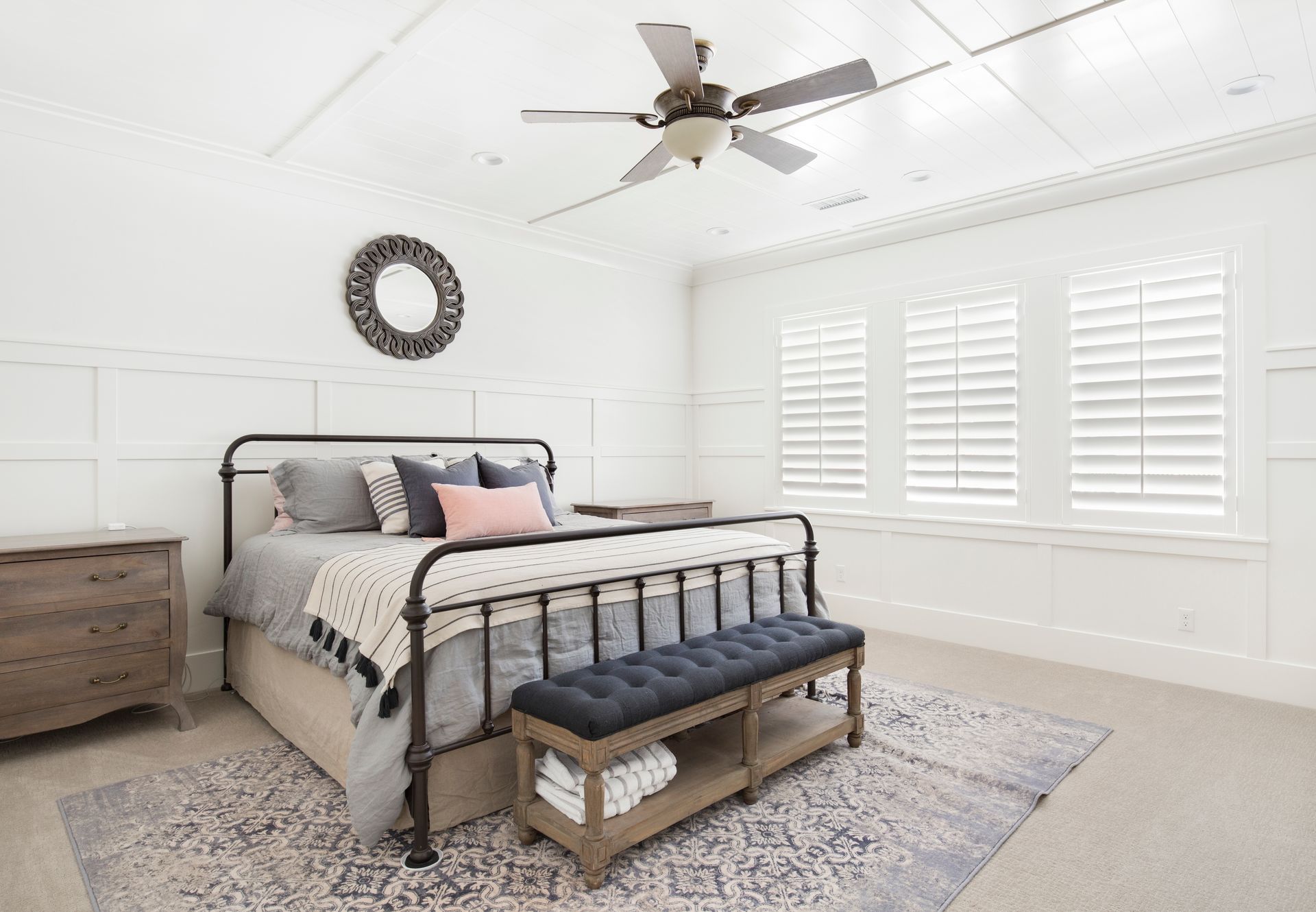 A bedroom with a bed , bench , nightstand and ceiling fan.