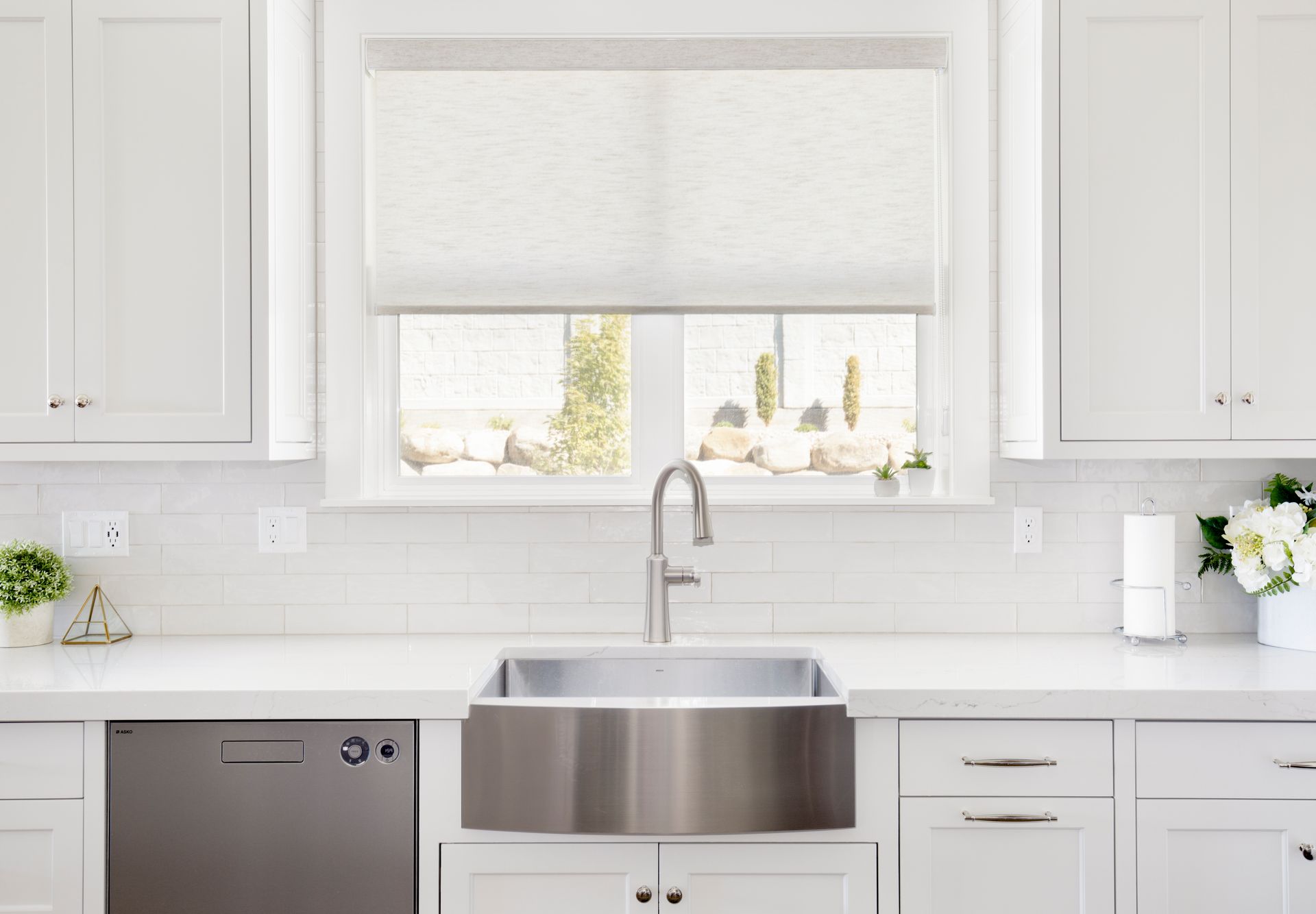 A kitchen with white cabinets , a stainless steel sink , a dishwasher , and a window.