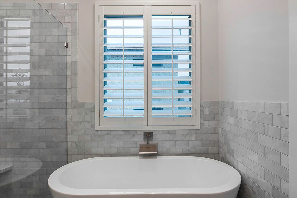 A bathroom with a bathtub and a window with shutters.