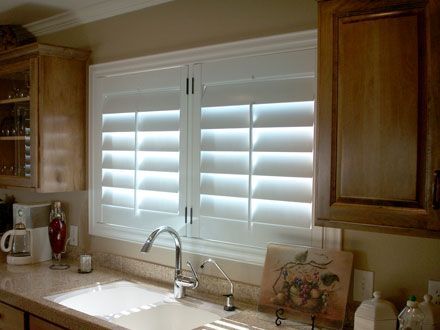 A kitchen with a sink and a window with white shutters.