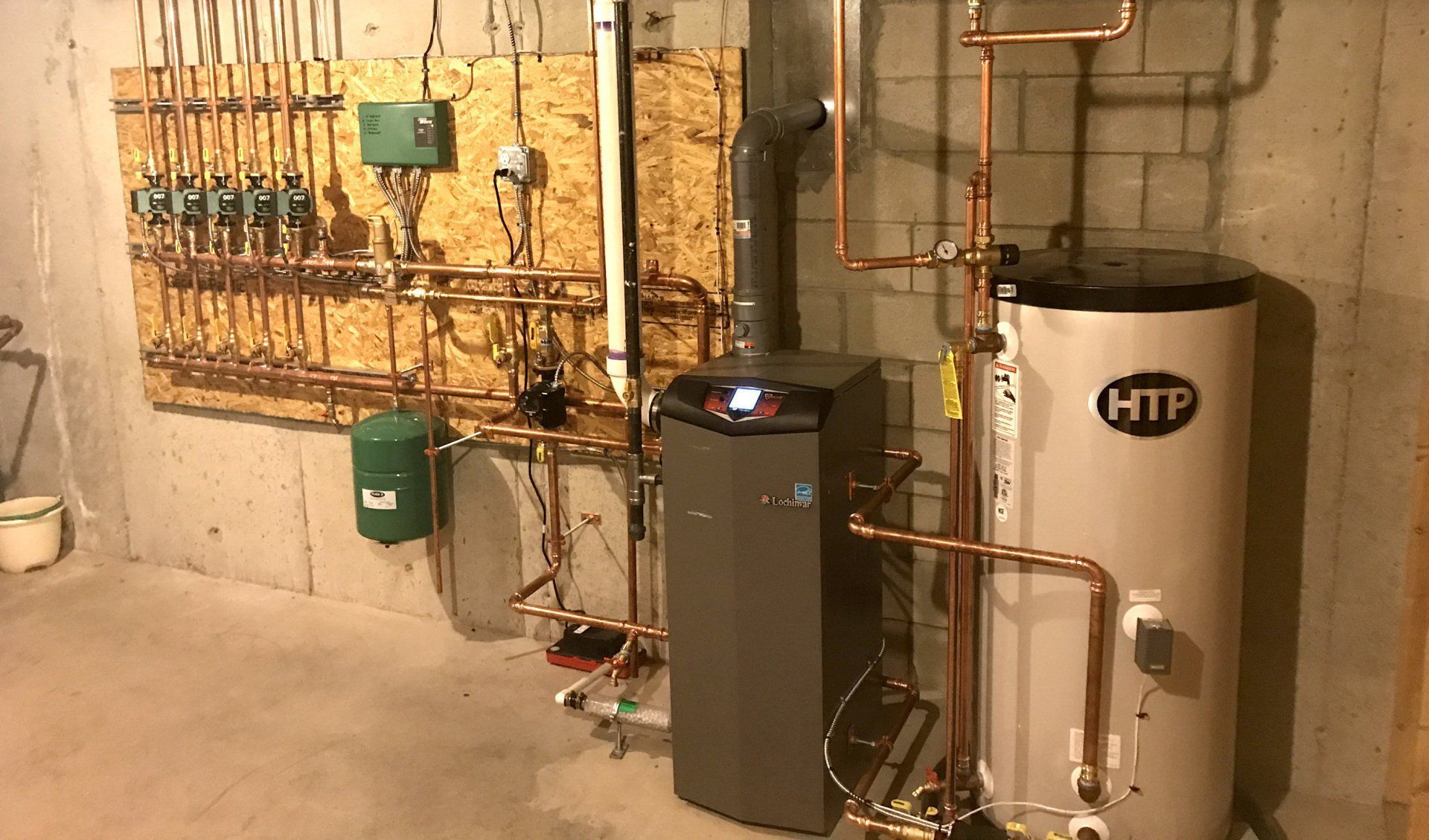 A basement with a heating system featuring a gray boiler, hot water tank, copper pipes, and a green expansion tank.