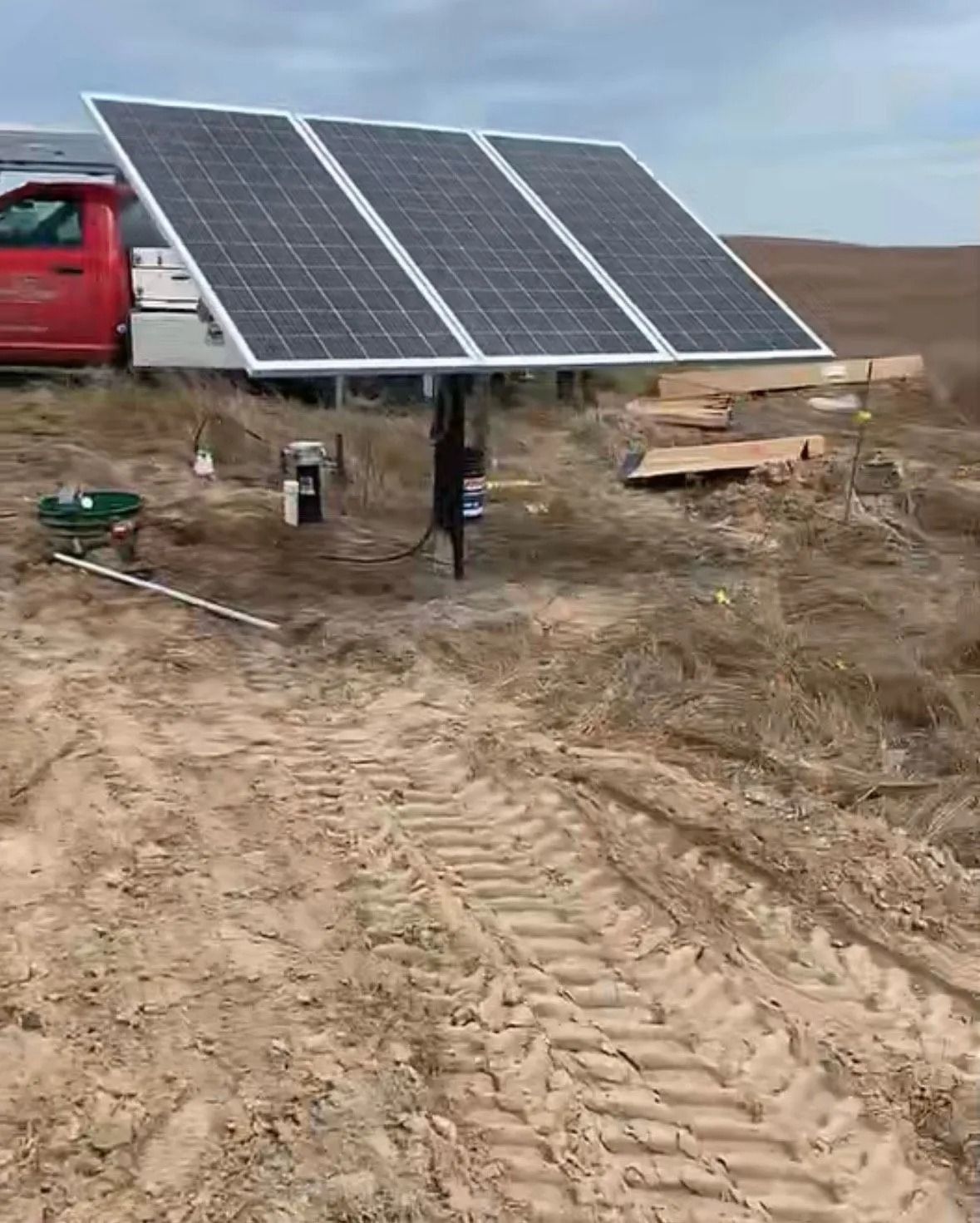 Ground-mounted solar panels in a rural field beside a red van and construction materials