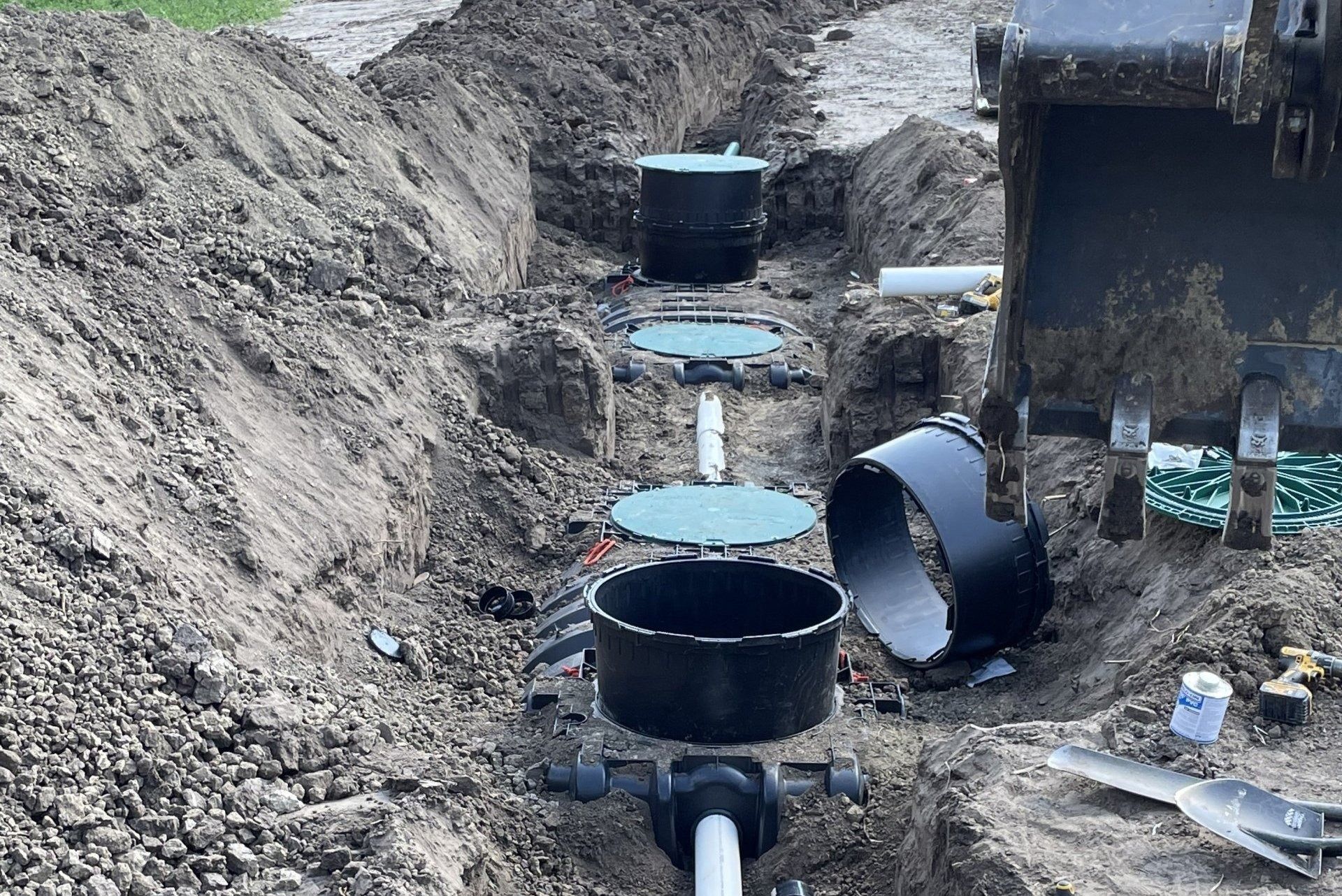Open utility trench with black pipes and circular manholes in a dirt construction site