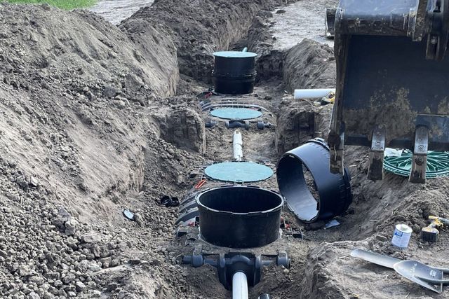 Construction site with black utility pipes laid in a dirt trench beside a concrete structure