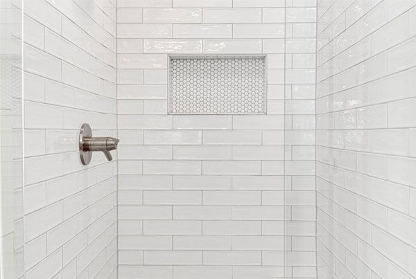A shower with white tiles and a stainless steel shower head.