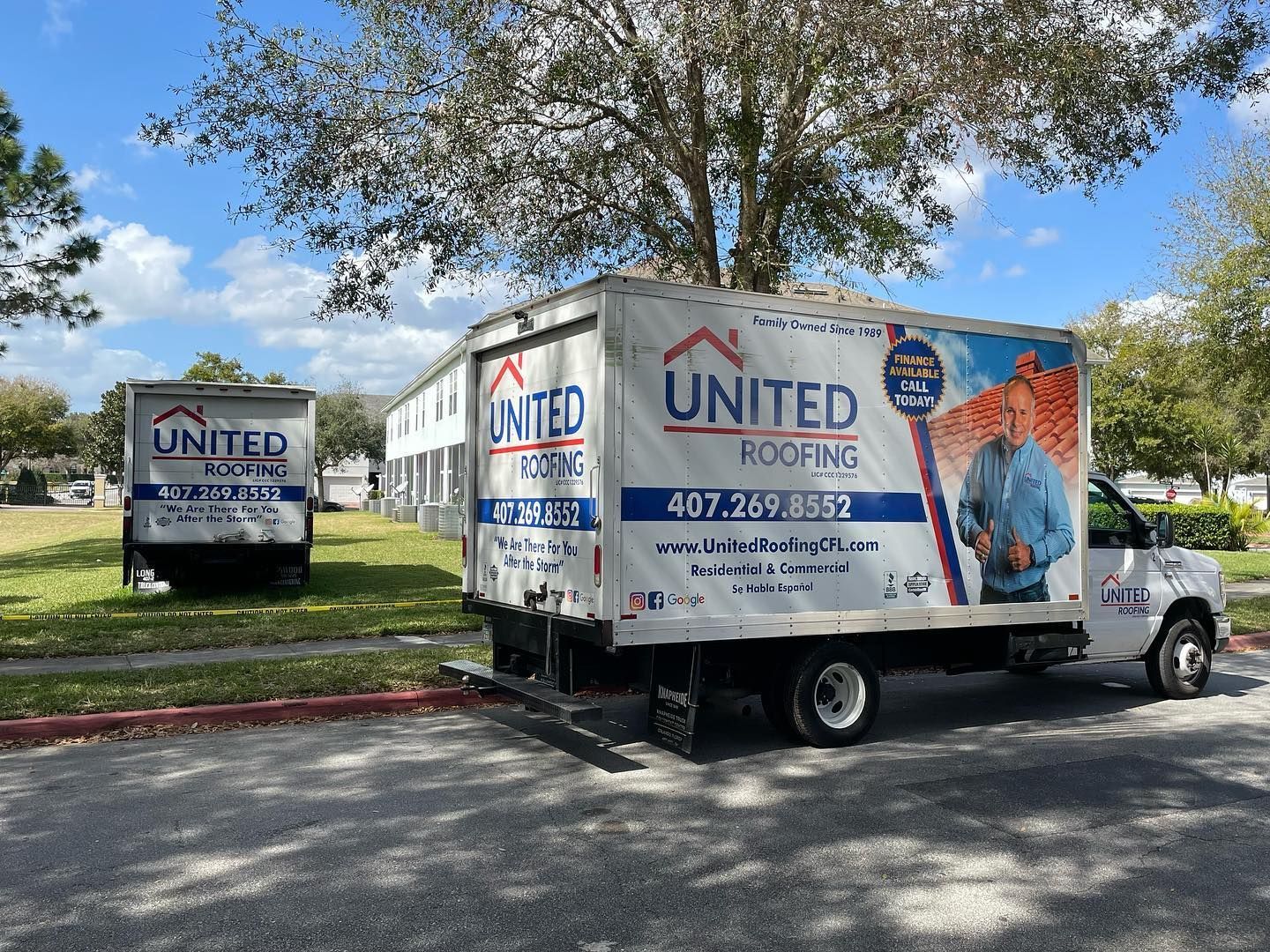 Two white United Roofing trucks parked on a paved area near a building with a lawn.