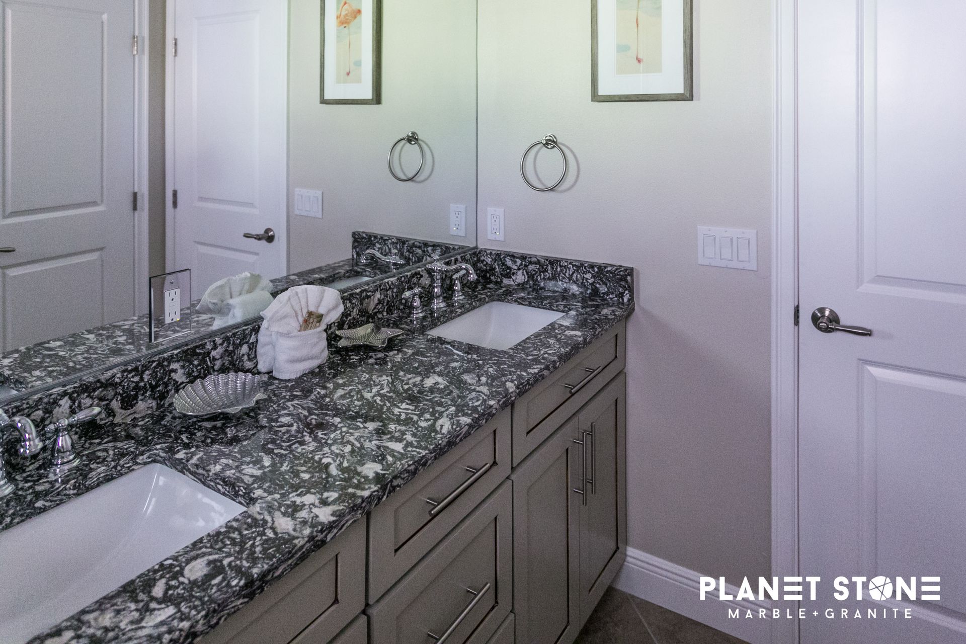Bathroom vanity with dark granite countertop, double sinks, and mirrors on a light wall.