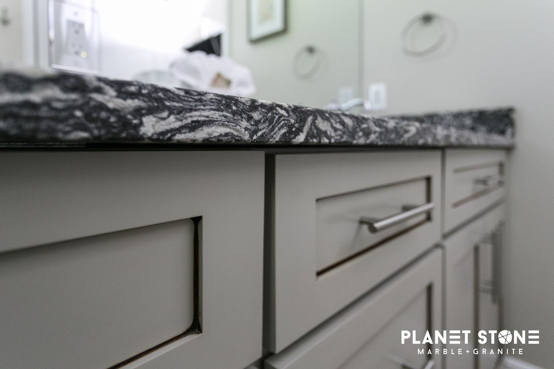 Close-up of a gray bathroom vanity with a dark stone countertop and metal drawer pulls