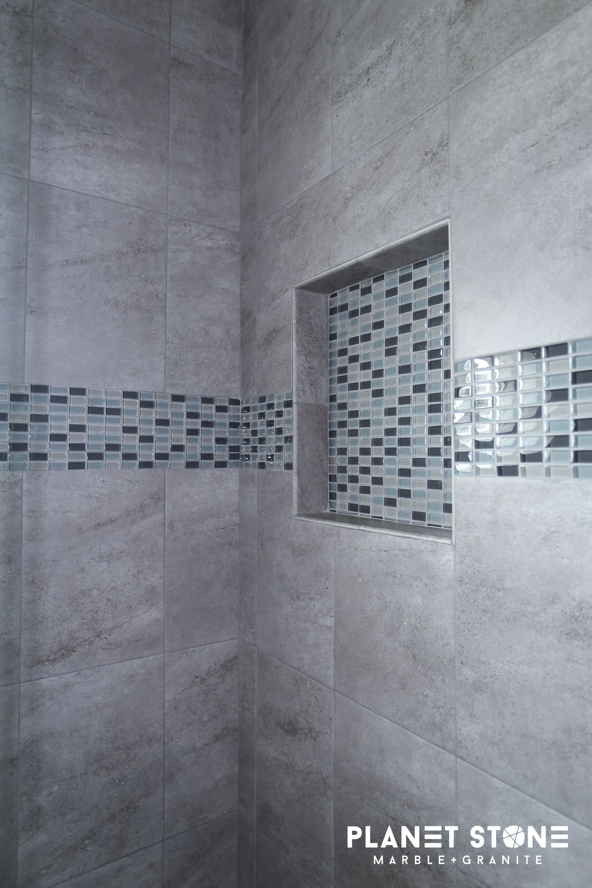 Gray tiled shower wall with a mosaic accent band and recessed shelf.