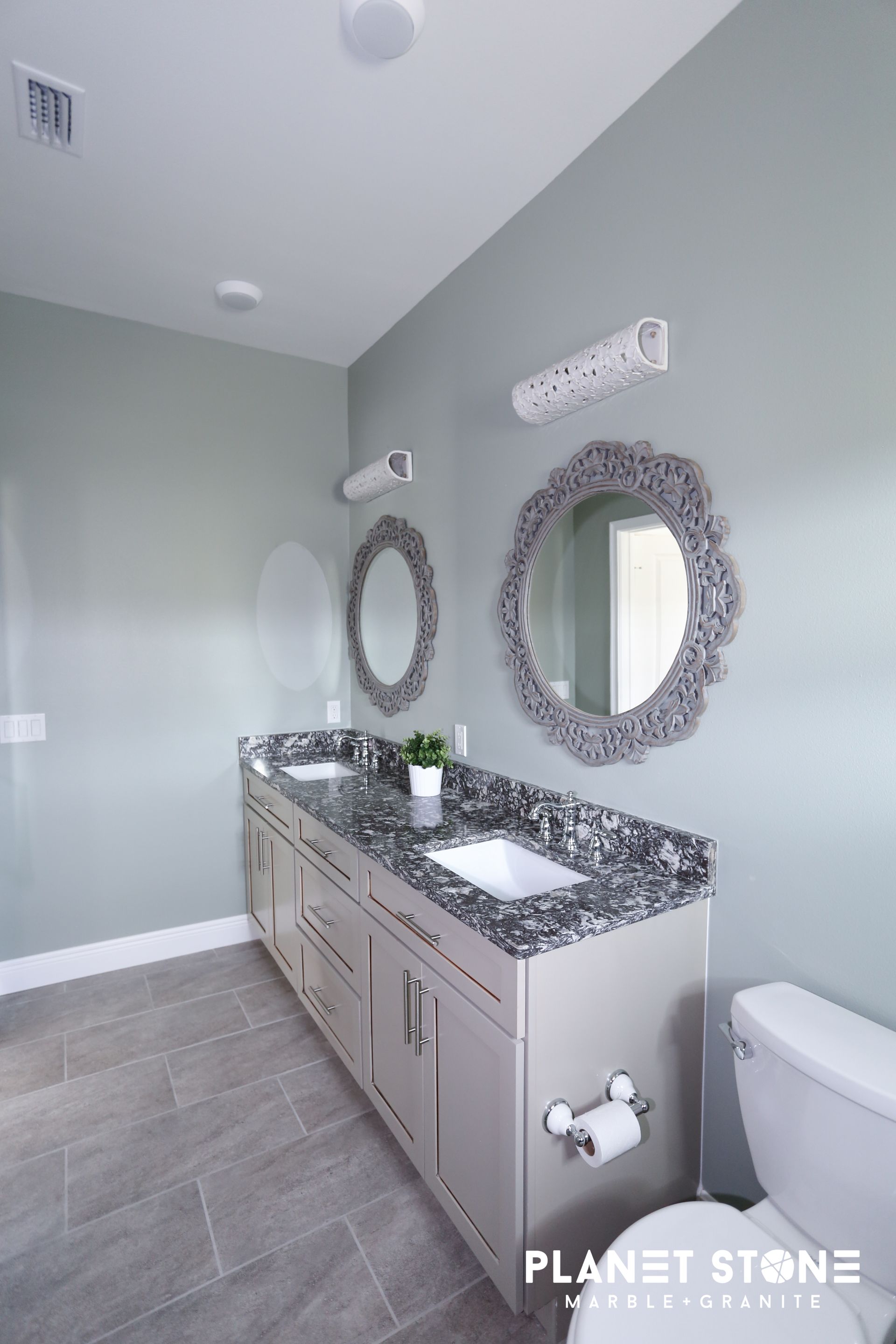 Modern bathroom with gray walls, mosaic vanity, round mirror, and white toilet
