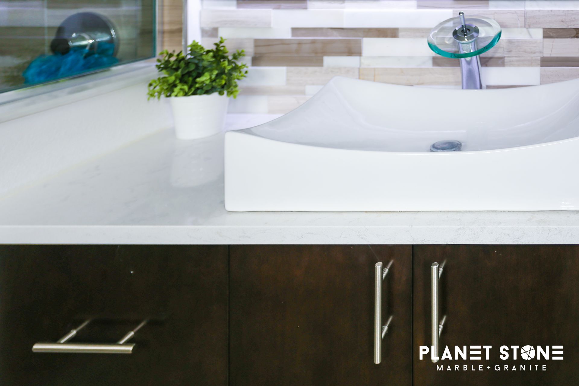 Modern bathroom vanity with white sink, dark wood cabinet, plant, and stone backsplash