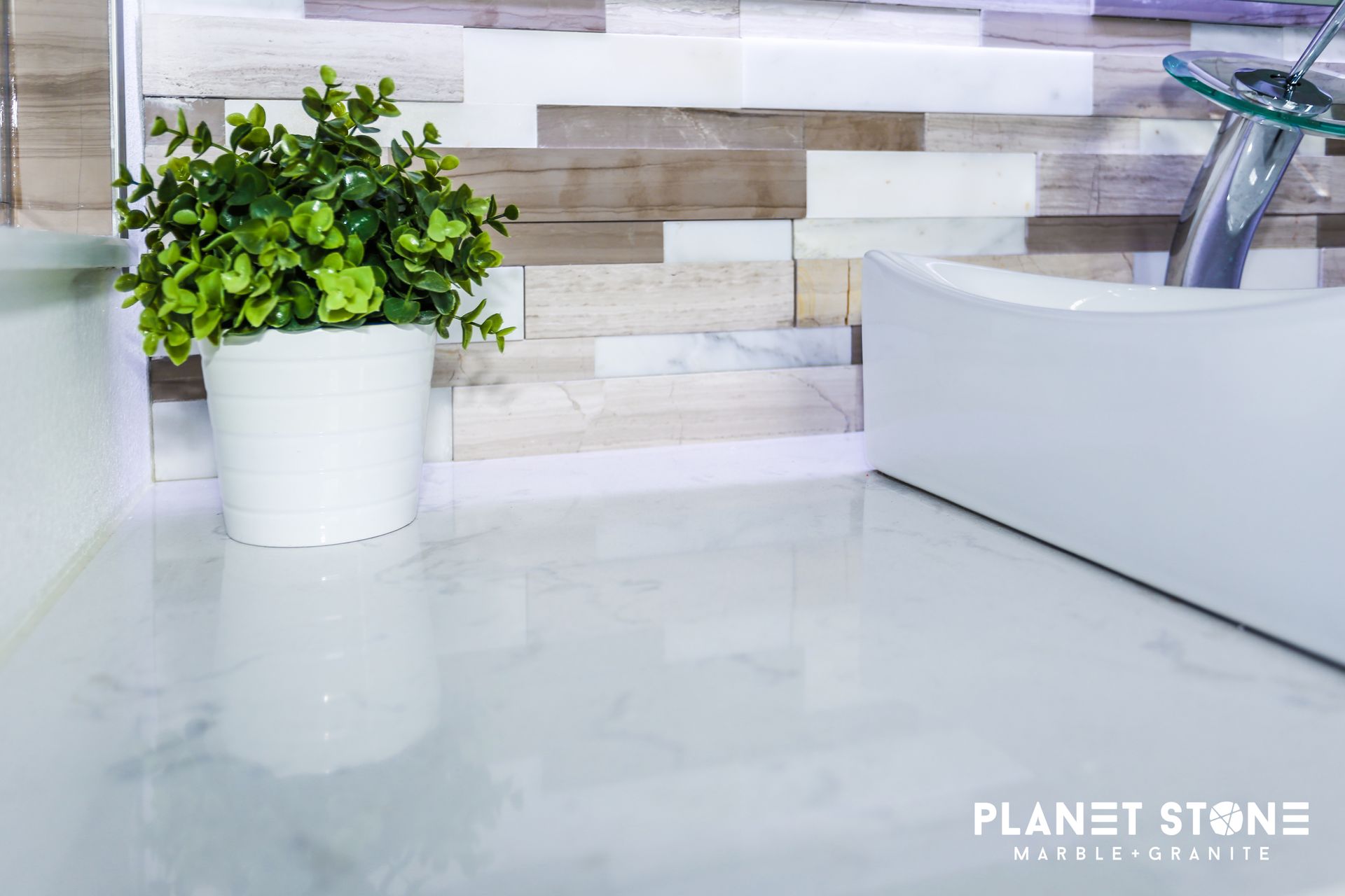 White glossy kitchen countertop with a potted plant and a sink against a tiled backsplash.