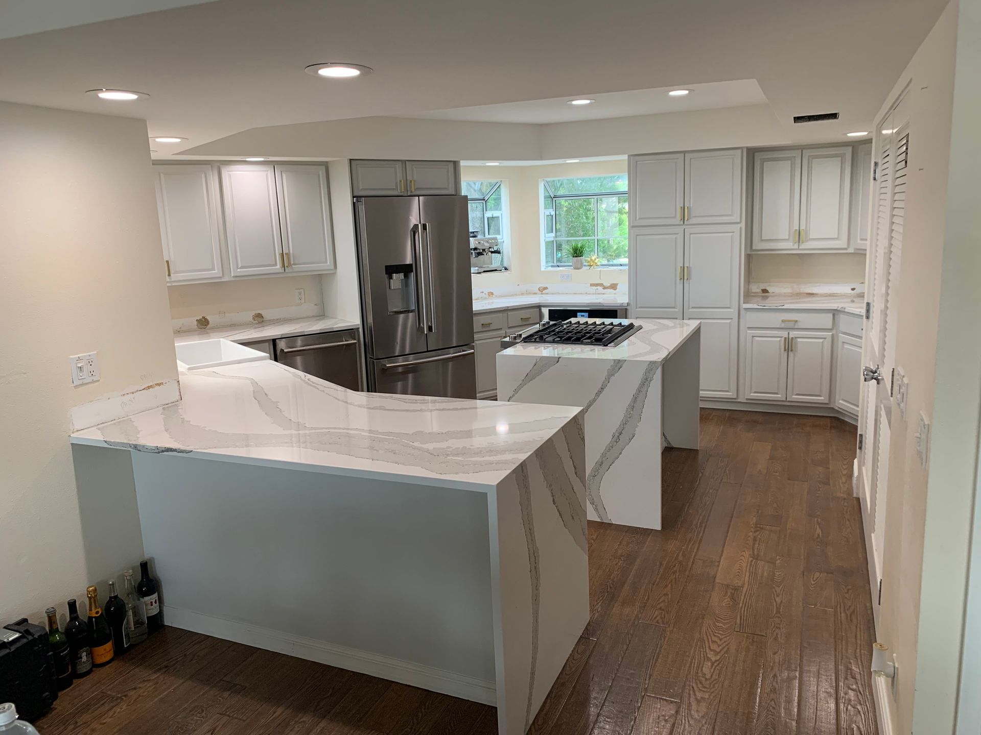 Modern white kitchen with quartz island, stainless steel fridge, and hardwood floors, viewed from the entryway