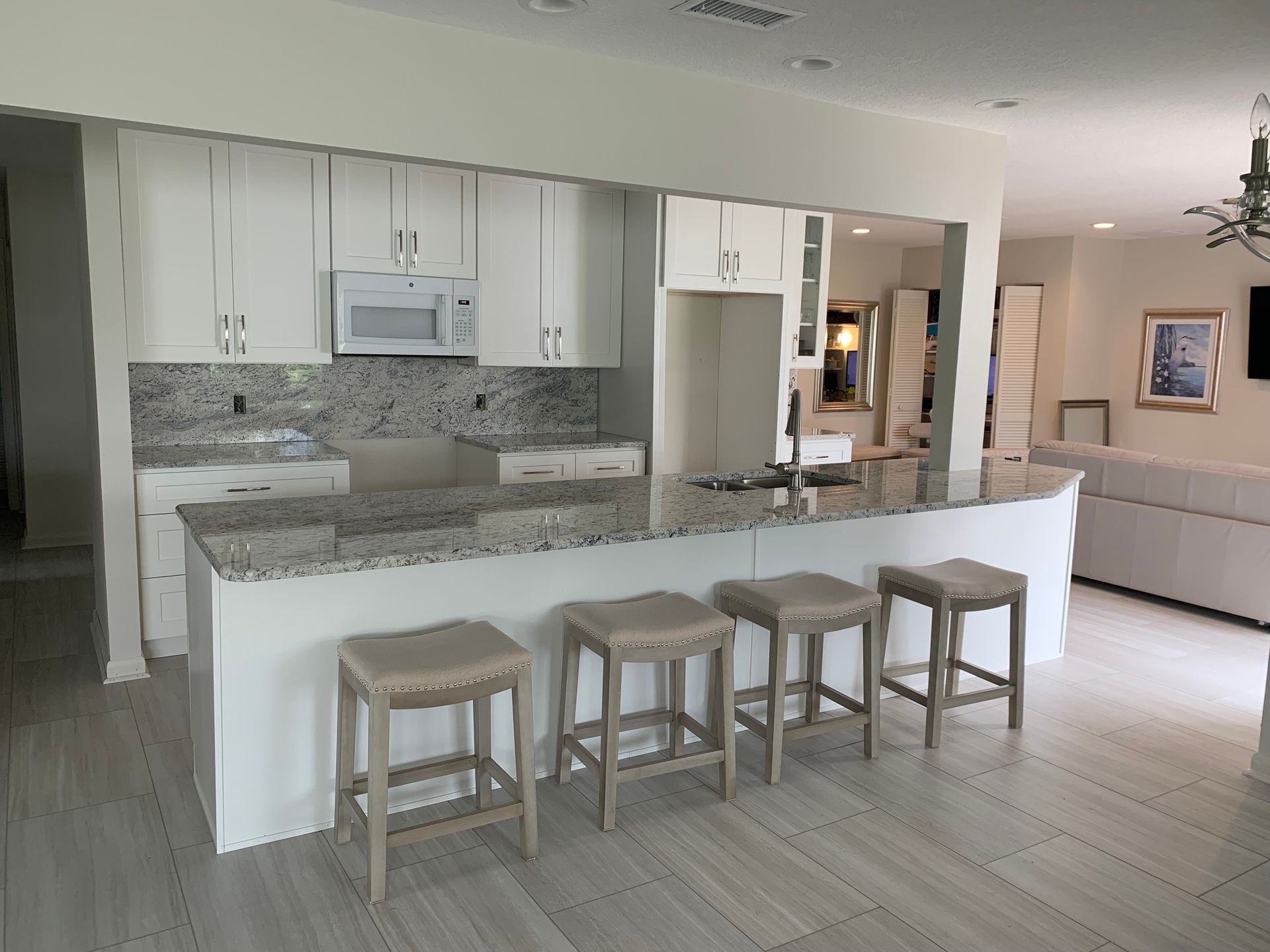 Bright modern kitchen with white cabinets, granite island, and four wooden stools