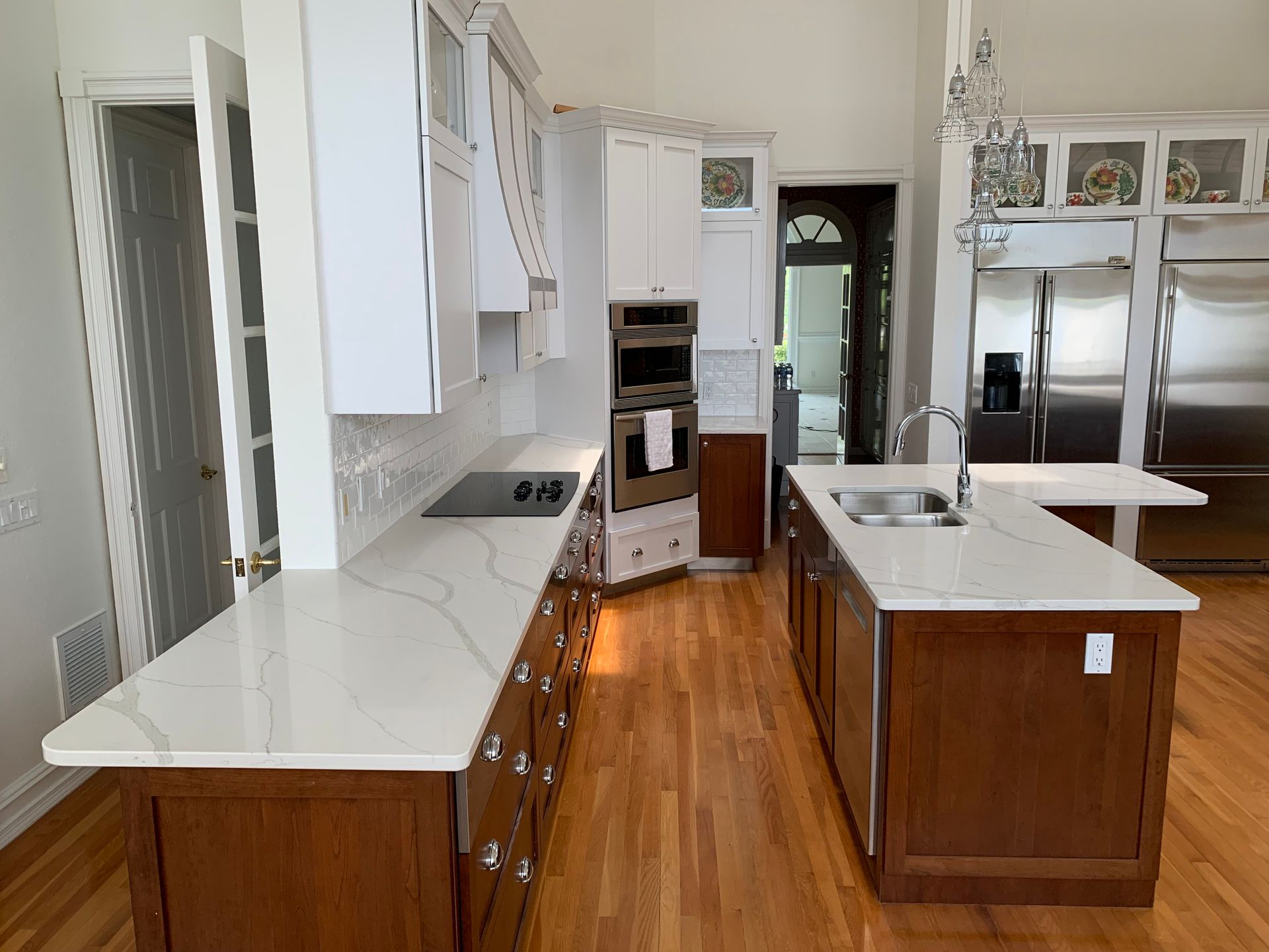 Bright kitchen with white cabinets, wood floors, island, stainless fridge, and a doorway in back