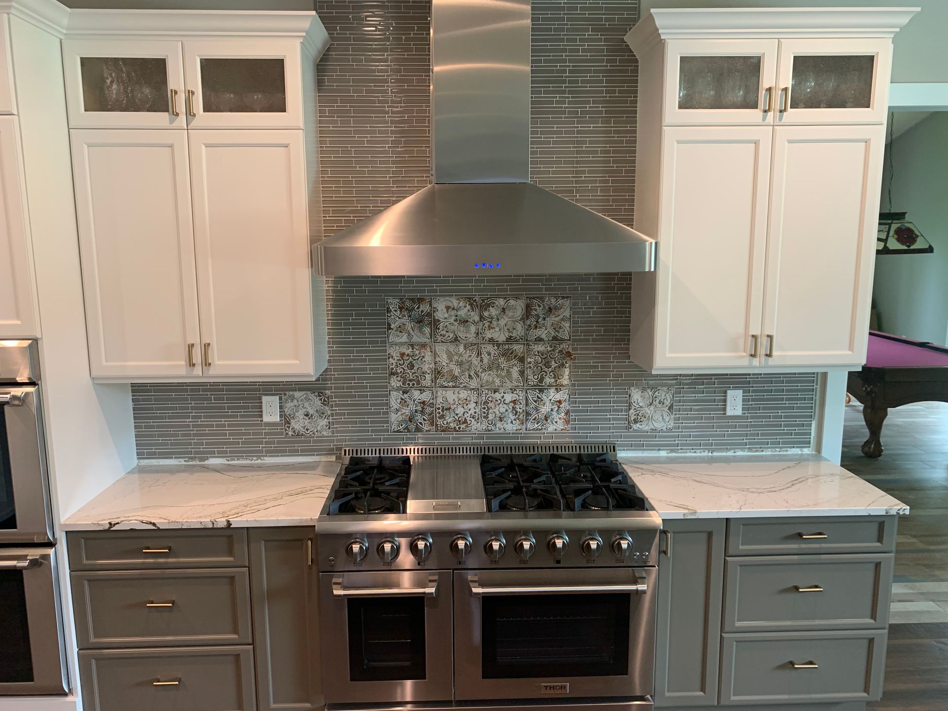 Modern kitchen with white cabinets, marble countertops, stainless steel range hood, and gas stove
