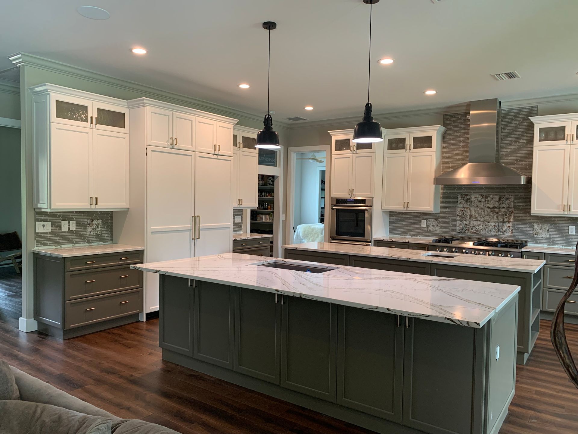 Modern kitchen with dark island, white cabinets, marble countertops, and stainless steel appliances.