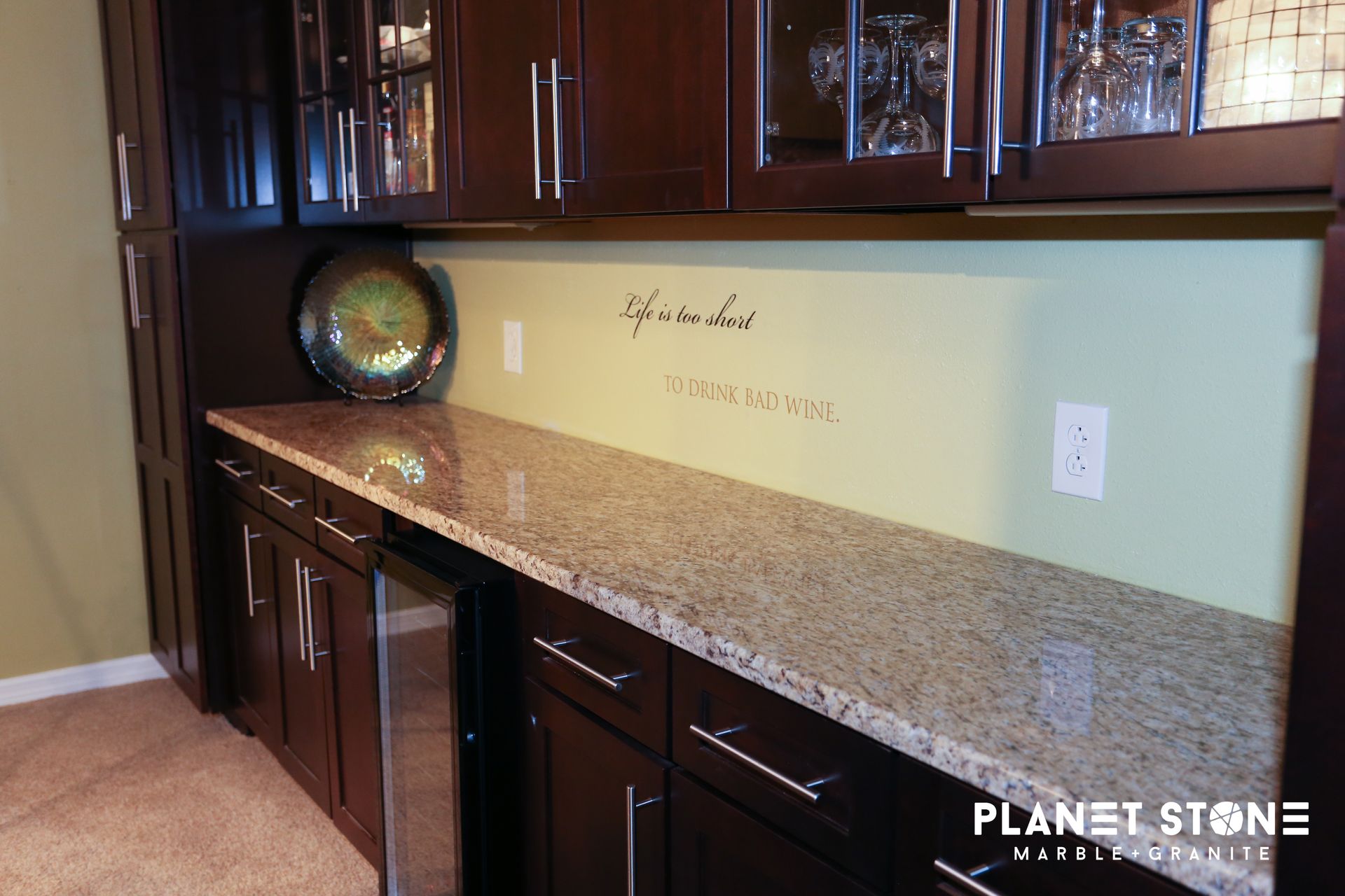 Built-in home office with dark wood cabinets, speckled granite countertop, and pale yellow backsplash wall.