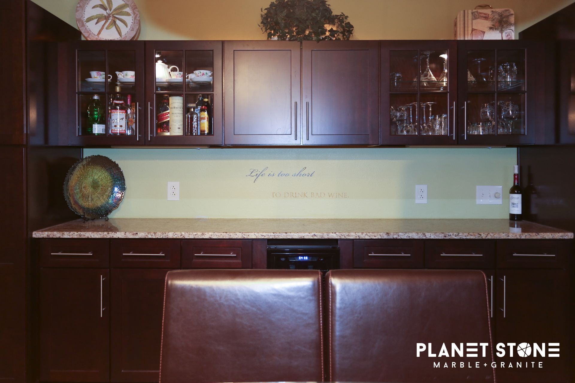Modern kitchen with dark wood cabinets, glass-front uppers, green backsplash, and two brown bar stools