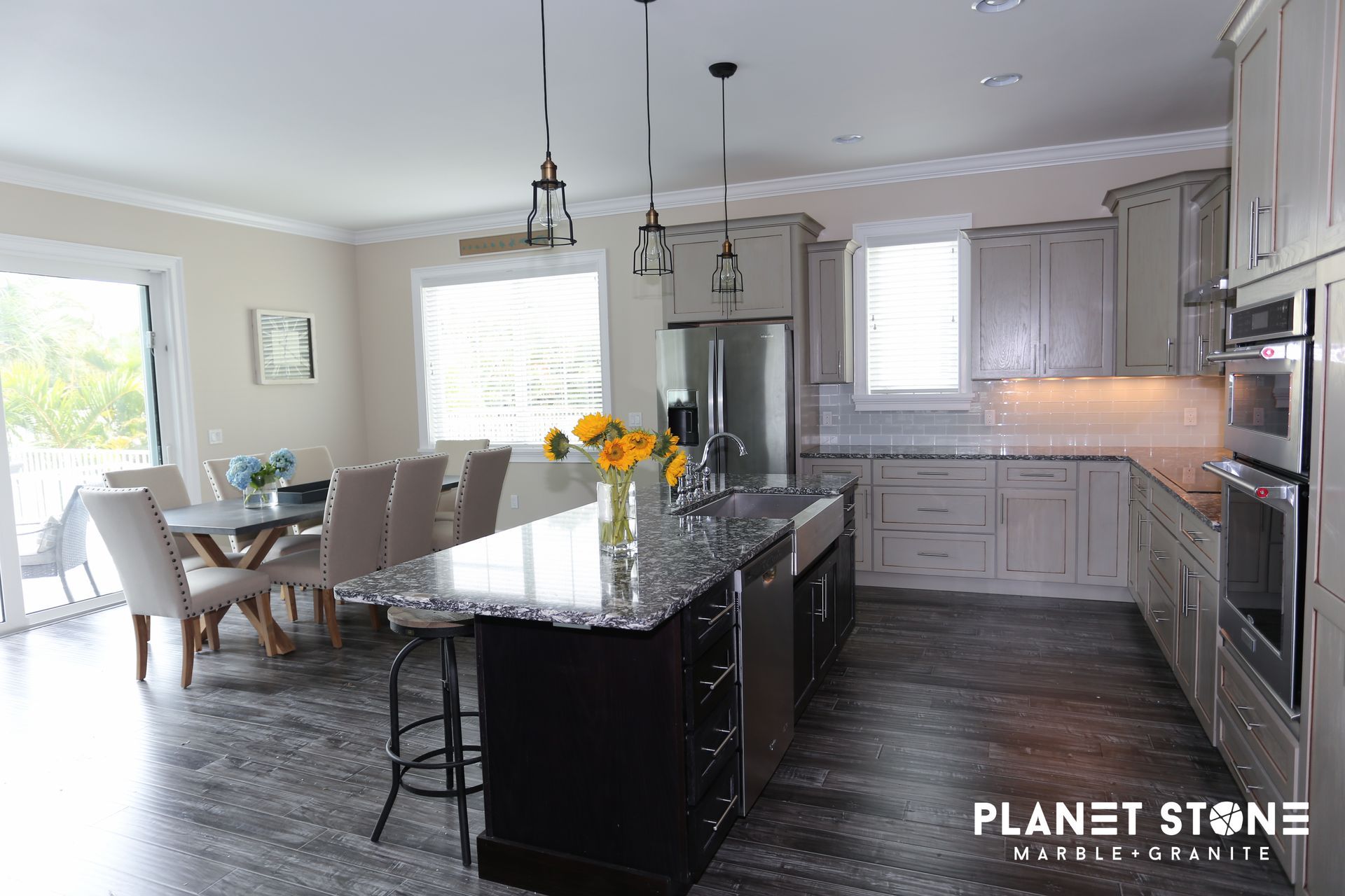 Modern kitchen and dining area with a dark island, gray cabinets, and a bright windowed nook
