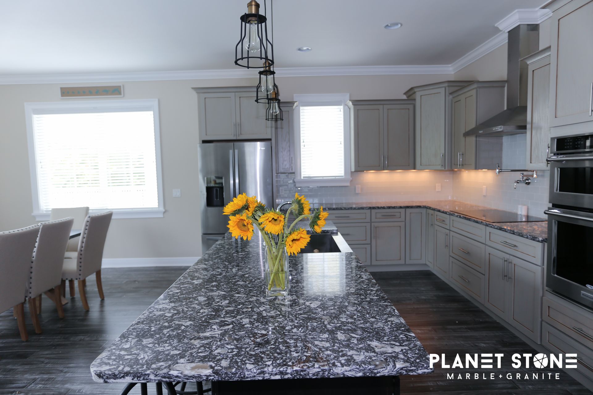 Modern kitchen with gray cabinets, granite island, stainless appliances, and yellow flowers on the counter