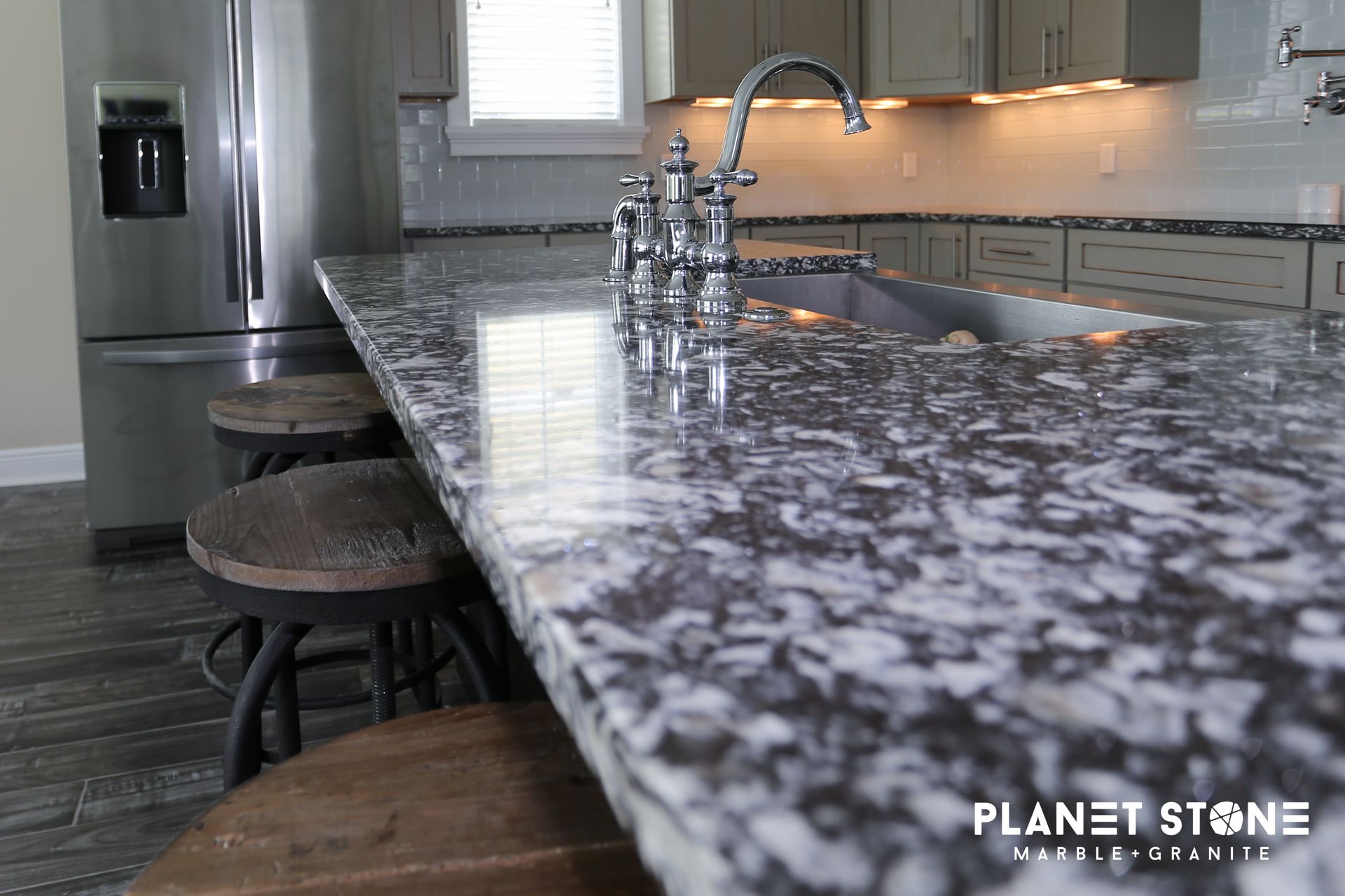 Modern kitchen with glossy granite island, sink, stools, and stainless steel appliances