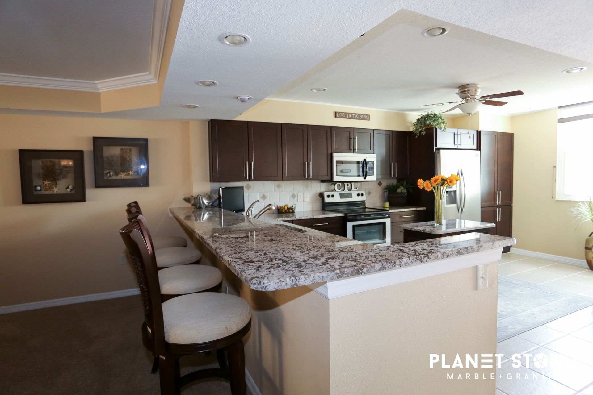Modern kitchen with granite island, dark cabinets, bar stools, and bright natural light