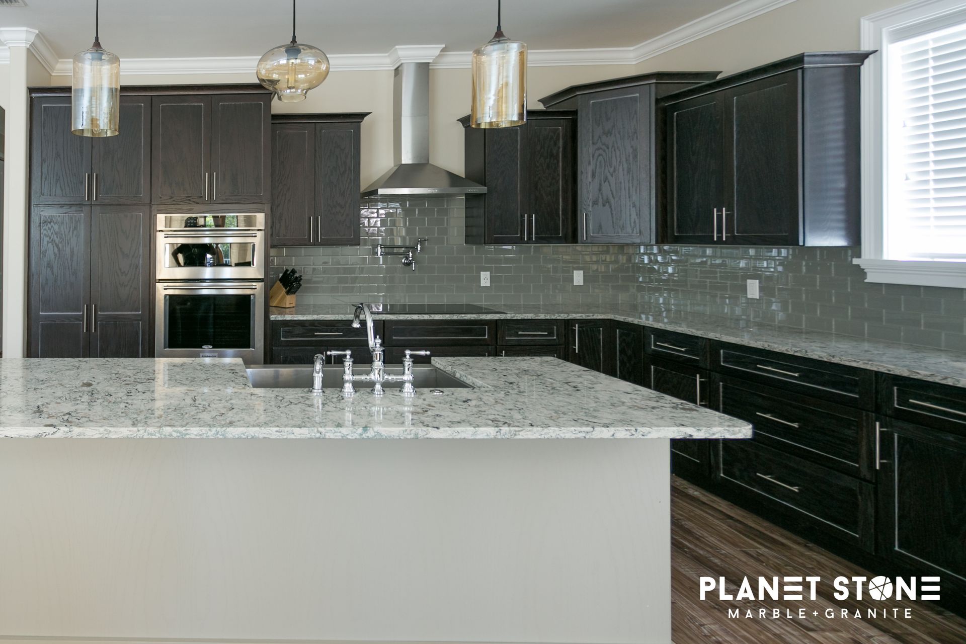 Modern kitchen with dark cabinets, gray tile backsplash, granite island, and pendant lights