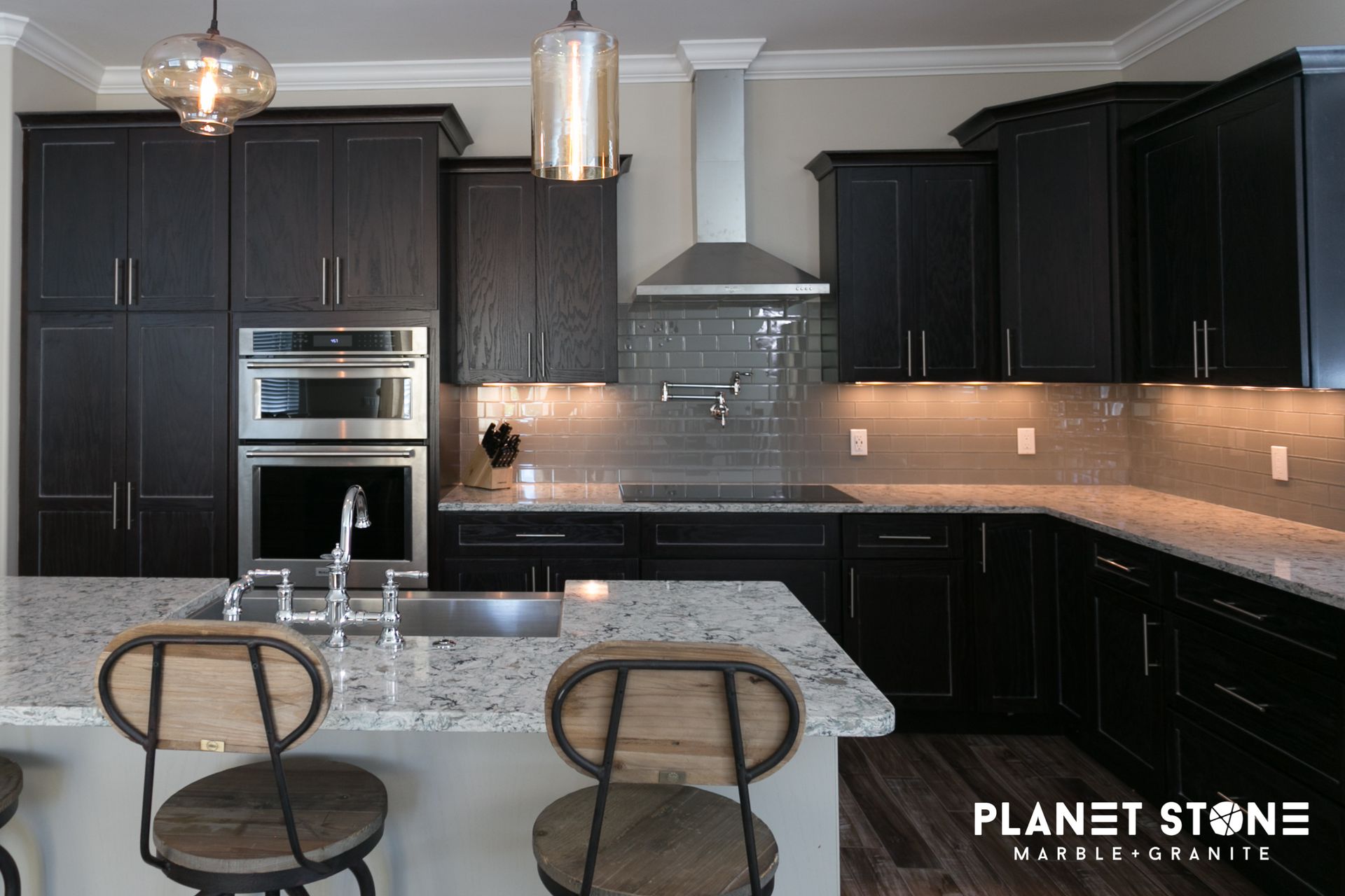 Modern kitchen with dark cabinets, marble island, stainless appliances, and two stools