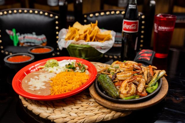 Mexican meal with rice, beans, chicken fajitas, chips, salsas, and Coca-Cola on a table