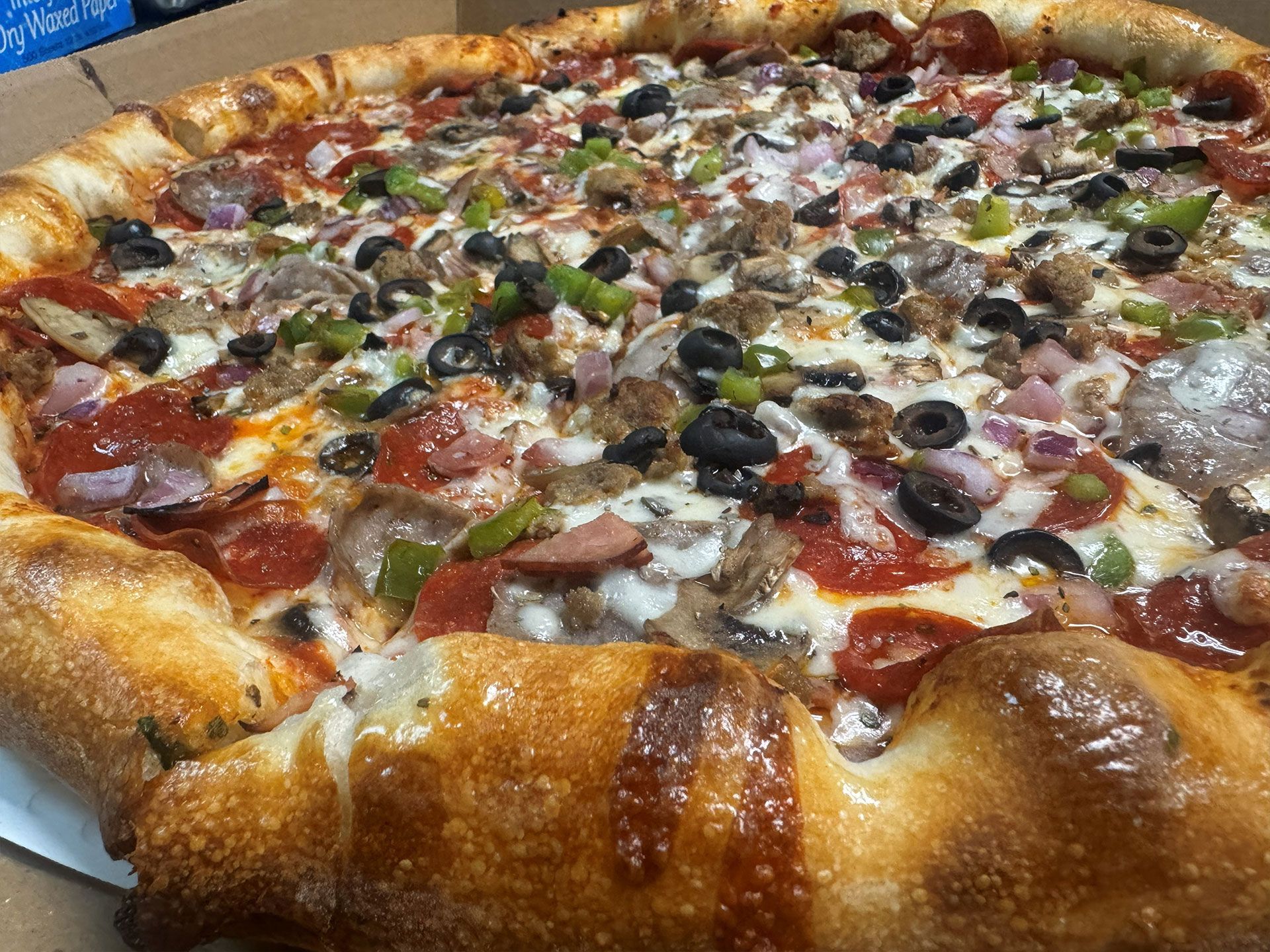 Pizza with various toppings, including pepperoni, olives, and green peppers, on a golden crust.