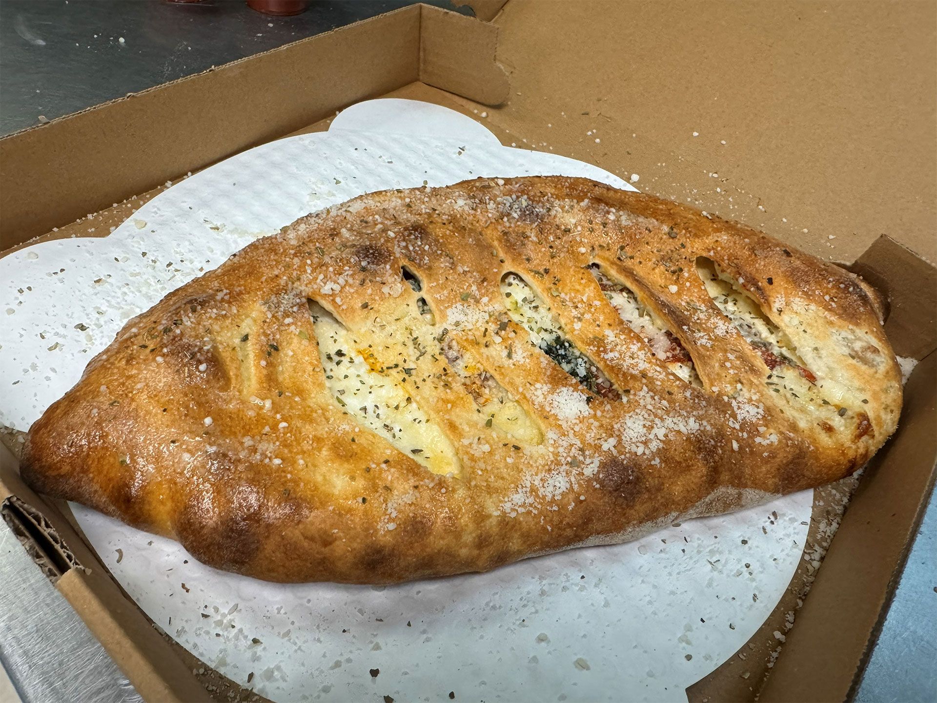 Calzone in a pizza box, golden brown with visible fillings and seasoning.