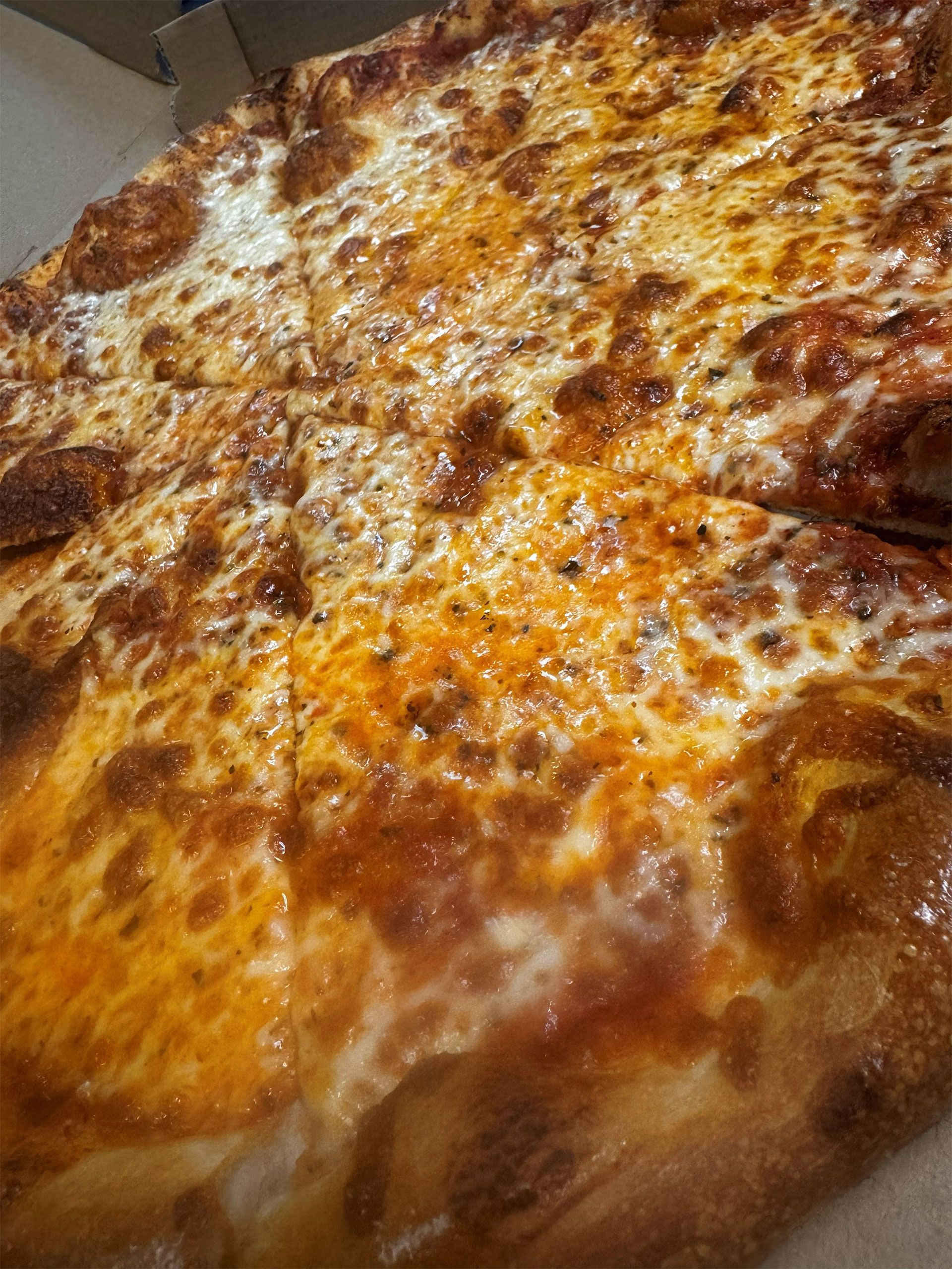 Close-up of a square pizza with melted cheese and red sauce. Some slices are cut.
