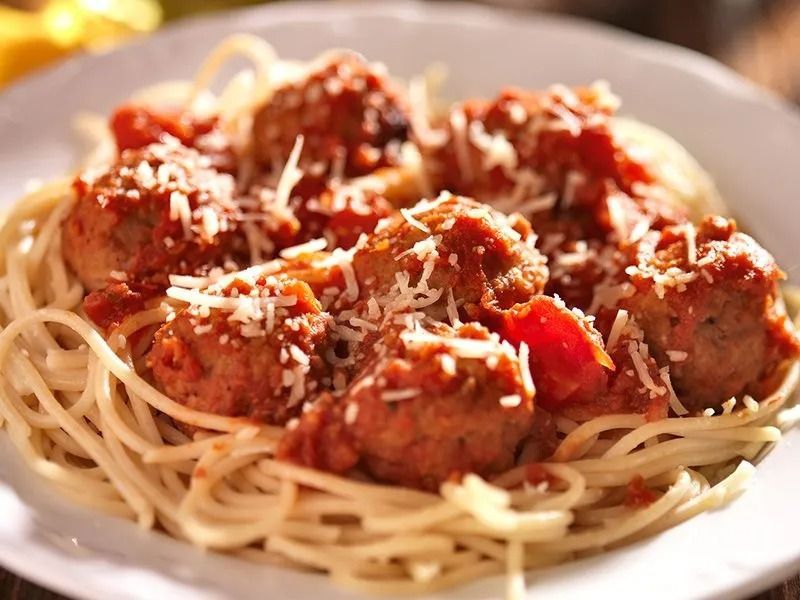 Spaghetti with meatballs in tomato sauce, sprinkled with Parmesan cheese, in a white bowl.