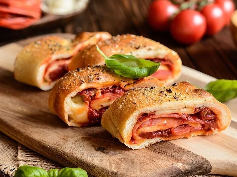 Three stuffed Italian bread rolls on a wooden board, with tomatoes and basil.